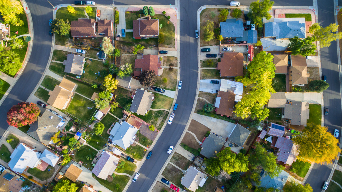 HOA Accounting Aerial photo of a residential suburban neighborhood. Numerous houses, green yards, and winding roads. Parked cars and trees with autumn foliage reflect a quiet community.