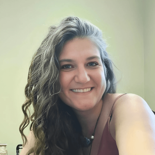 Smiling woman with short blonde hair and friendly brown eyes wearing a flowered blouse complementing her natural aesthetic and inviting expression.
