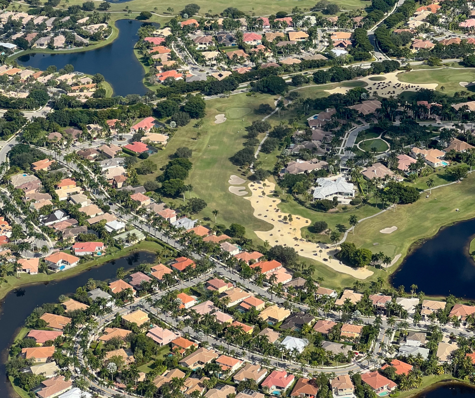 drone neighborhood Aerial view of a vibrant suburban community featuring homes with pools, manicured lawns, and curved streets, alongside a dense natural forest at sunset.